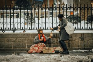 a woman gives food to a a young homeless man on the street on a snowy day